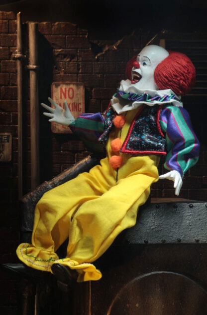 Clown doll with red hair and yellow outfit sitting on a metal surface against a dark brick wall.